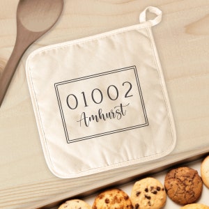 May include: A white cotton pot holder with a black border and the text "01002 Amherst" printed on it.