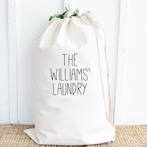 May include: A white canvas laundry bag with a drawstring closure. The bag has black text that reads "THE WILLIAMS' LAUNDRY".