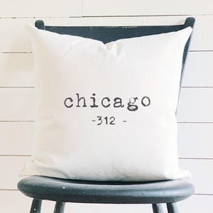 May include: White pillow with black text that reads "chicago -312-" on a black chair.