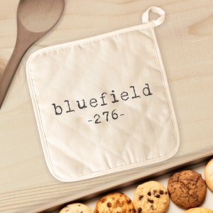 May include: A white cotton pot holder with a black text design that says "bluefield -276-"