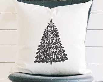May include: A white square pillow with a black Christmas tree design. The tree is filled with the words "Joy, Peace, Bright, Cheers, Merry Christmas" in a decorative font. The pillow is sitting on a black chair.