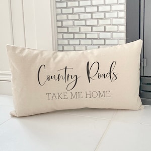May include: A white throw pillow with the text "Country Roads Take Me Home" in black cursive font.