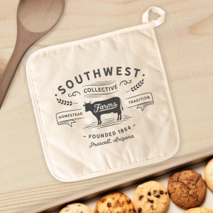 May include: A white cotton pot holder with a black and white logo that says "Southwest Collective Farms" with the text "Homestead, Tradition, Founded 1864 - Prescott, Arizona".