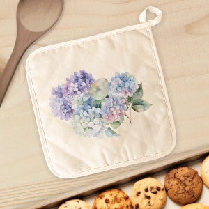 May include: A white cotton pot holder with a floral design featuring blue and purple hydrangeas. The pot holder has a loop for hanging.