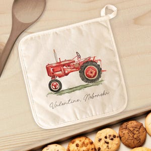 May include: Red vintage tractor with a white pot holder featuring the text "Valentine, Nebraska".