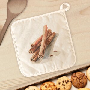 May include: A square, off-white pot holder with a loop for hanging. The pot holder features a watercolor illustration of several cinnamon sticks. The pot holder is on a light wooden surface, with a wooden spoon and a tray of cookies visible.