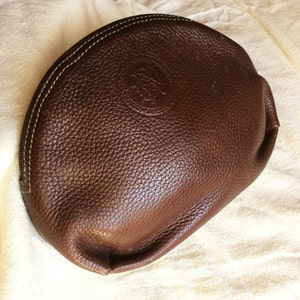 May include: A brown leather half-moon shaped cosmetic bag with a stitched edge and a small embossed logo.