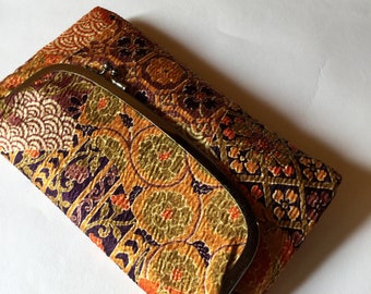 May include: A vintage-style clutch purse with a gold-toned clasp. The fabric is a rich orange and brown with a floral pattern.
