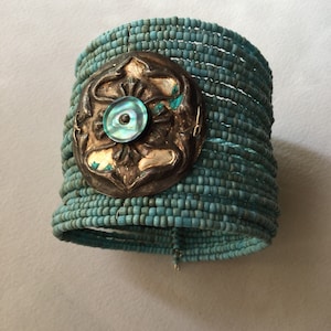 Può includere: Un braccialetto di perline turchesi con un ciondolo decorativo in argento e turchese. Il ciondolo ha un design circolare con un centro turchese.