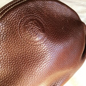 May include: A brown leather purse with a stitched edge and a circular embossed logo.
