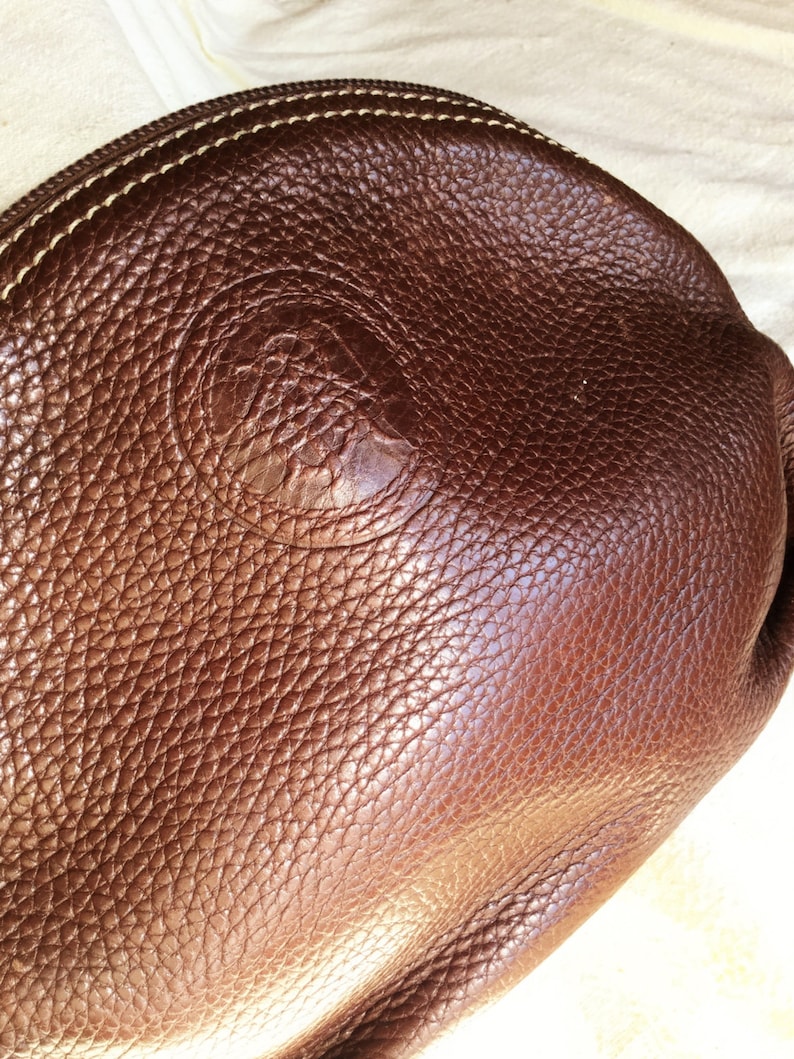 May include: A brown leather purse with a stitched edge and a circular embossed logo.