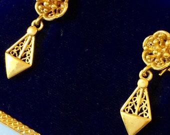 May include: A pair of gold filigree earrings with a diamond-shaped pendant and a floral design. The earrings are displayed in a blue velvet box.