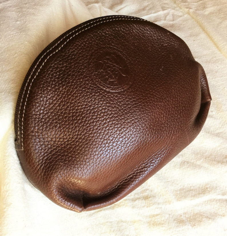 May include: A brown leather half-moon shaped cosmetic bag with a stitched edge and a small embossed logo.