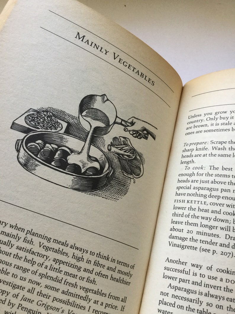 May include: A vintage cookbook open to a page titled "Mainly Vegetables". The page features a black and white illustration of a person cooking vegetables in a pot on a stovetop.