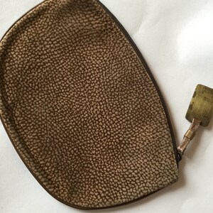 May include: A brown suede zippered pouch with a small metal tag attached to the zipper pull.