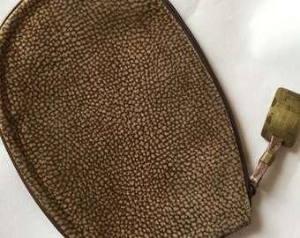 Może przedstawiać: Brązowa skórzana kosmetyczka zapinana na zamek błyskawiczny z małą metalową zawieszką przyciągniętą do suwaka.