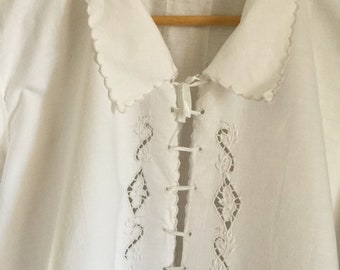 May include: White cotton shirt with a scalloped collar and intricate lace embroidery on the front. The embroidery features a diamond pattern with floral details.