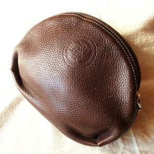 May include: A brown leather cosmetic bag with a white stitching detail and a small embossed logo.