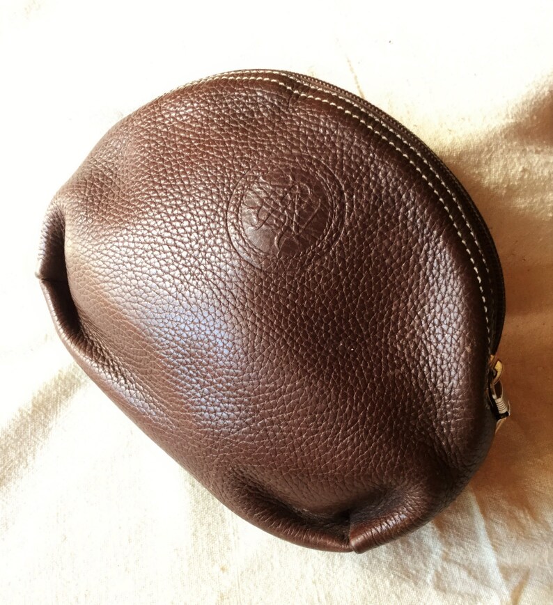 May include: A brown leather cosmetic bag with a white stitching detail and a small embossed logo.