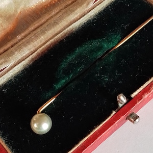 Peut inclure: Un fermoir de cravate en or avec une seule perle sur un fond de velours vert foncé dans une boîte en velours rouge.