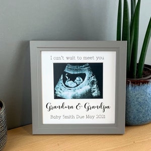 May include: A gray picture frame with a white mat and a black and white ultrasound image inside. The text "I can't wait to meet you" is printed above the image. The text "Grandma & Grandpa" is printed below the image, along with the text "Baby Smith Due May 2021".