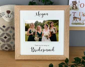 May include: A wooden picture frame with a white mat and a photo of four women in green dresses. The text "Megan" is printed at the top of the frame and "Thank you for being my Bridesmaid" is printed at the bottom.
