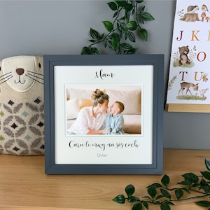 May include: A gray picture frame with a white mat and a photo of a mother and child. The text "Mam" and "Caru ti mwy na sos coch" is printed on the mat. The text "Dylan" is printed below the Welsh phrase.