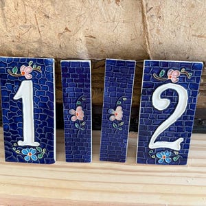 Peut inclure: Quatre carreaux en céramique rectangulaires avec un fond bleu profond à motif de briques. Deux carreaux présentent les chiffres blancs 1 et 2, tandis que deux carreaux plus étroits arborent des motifs floraux peints à la main.