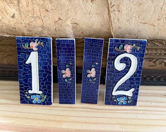 May include: Four rectangular ceramic tiles featuring a deep blue brick-patterned background. Two tiles display the white numbers 1 and 2, while two narrower tiles feature hand-painted pink and blue floral motifs with green stems and leaves.