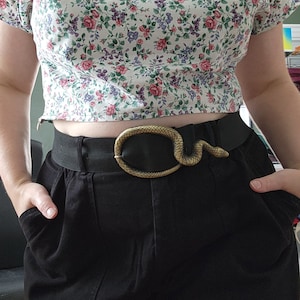May include: A black high-waisted skirt with a snake-shaped belt buckle. The belt is black and the buckle is gold.