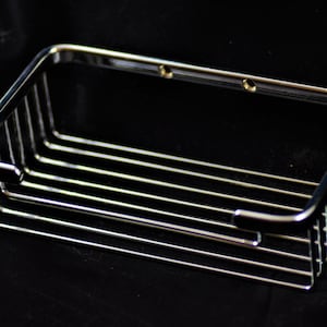 May include: A chrome-plated metal bathroom shelf with a rectangular shape and a wire mesh design. The shelf has two holes on the top for mounting.