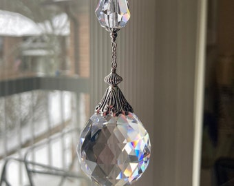 May include: A crystal suncatcher with a silver chain and two crystal beads. The larger crystal is faceted and reflects light.