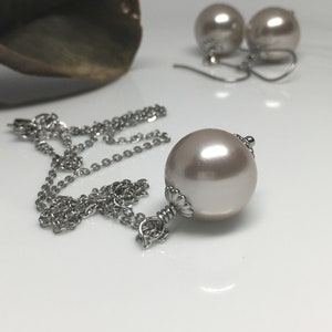 May include: A silver chain necklace with a large, off-white pearl pendant. The pendant is attached to the chain with a silver clasp. Two matching pearl earrings are also included.