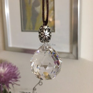 May include: A clear crystal ball hanging from a brown cord with a silver charm featuring a floral design. The charm has the text "MyOnlyChoice" on it.