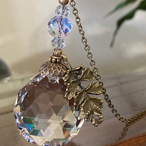 May include: A crystal pendant necklace with a faceted crystal ball, a bronze acorn charm, and a bronze leaf charm. The necklace has a bronze chain and crystal beads.