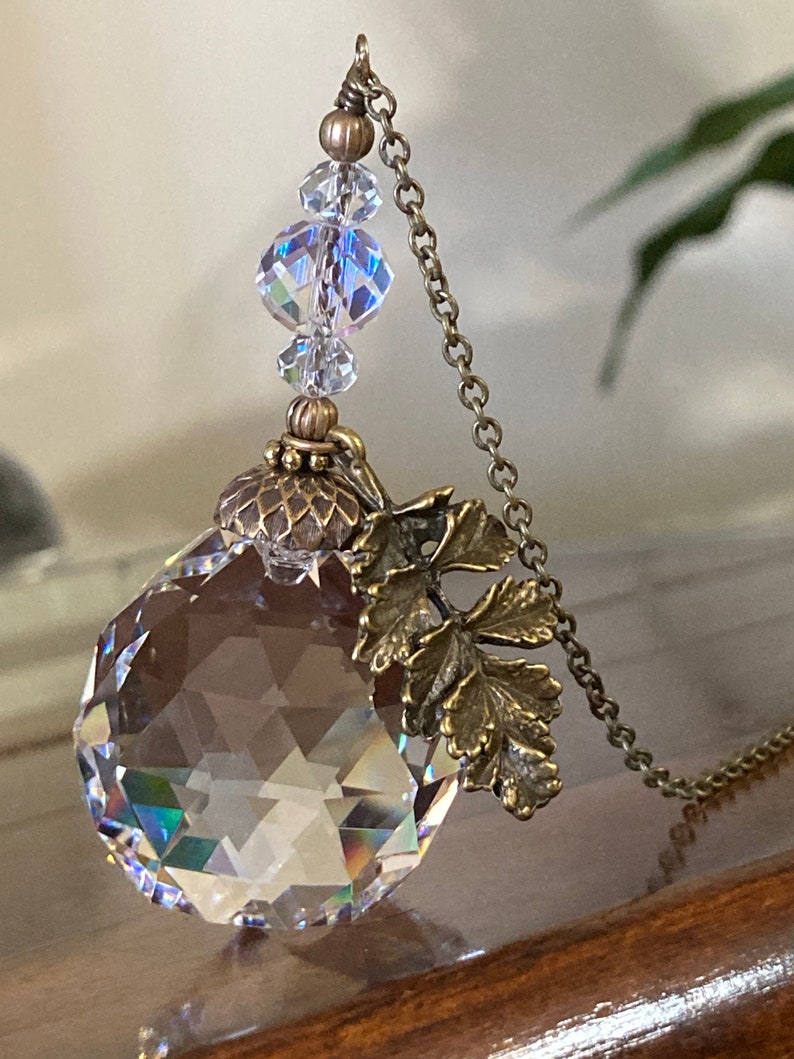 May include: A crystal pendant necklace with a faceted crystal ball, a bronze acorn charm, and a bronze leaf charm. The necklace has a bronze chain and crystal beads.