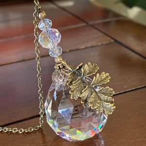 May include: A crystal prism with a gold chain and a leaf-shaped charm. The prism is faceted and reflects light.