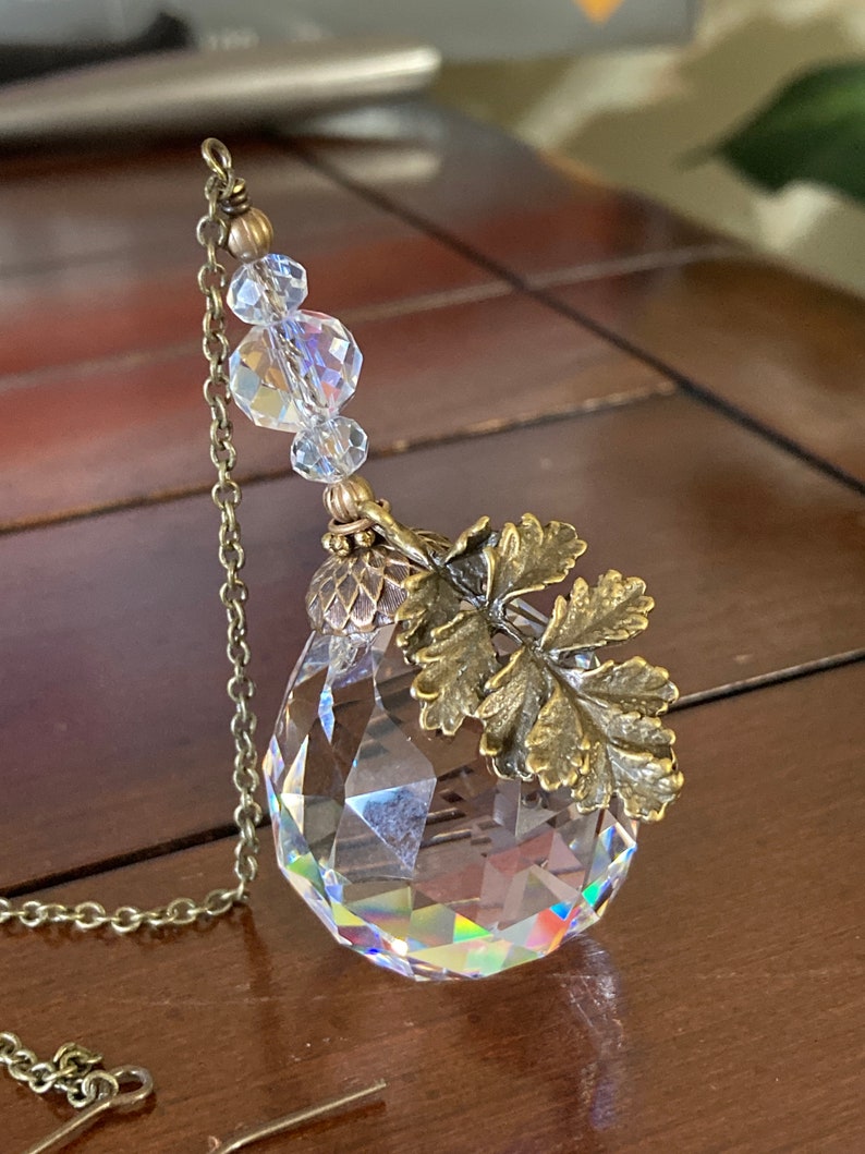 May include: A crystal prism with a gold chain and a leaf-shaped charm. The prism is faceted and reflects light.