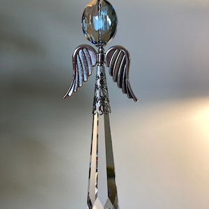 May include: A crystal angel ornament with a clear teardrop-shaped crystal and a blue crystal sphere at the top. The angel has silver wings.
