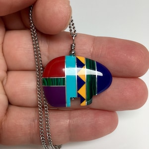 May include: A silver chain necklace with a colorful bear pendant. The pendant is made of red, blue, green, purple, yellow, and turquoise stones.