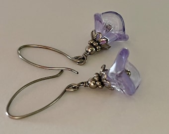 May include: A pair of silver earrings with lavender glass flower charms. The flowers have a delicate, slightly translucent appearance.