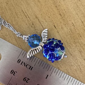 Op de afbeelding: Een zilveren ketting met een blauwe glazen kraal en een zilveren engelenvleugel bedel. De kraal is ongeveer 2,5 cm in diameter.