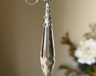 May include: A pair of silver dangle earrings with a clear crystal teardrop pendant. The earrings have a silver wire loop and a silver bead.