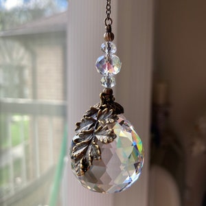 May include: A crystal suncatcher with a clear glass orb and a decorative metal leaf design. The orb is suspended from a chain with clear crystal beads.