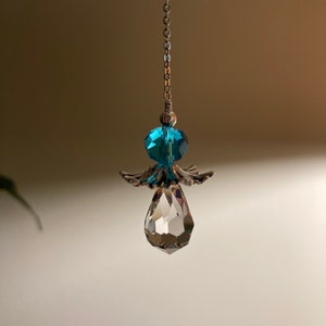 May include: A crystal teardrop pendant with a silver angel wing design and a blue crystal bead. The pendant hangs from a silver chain.
