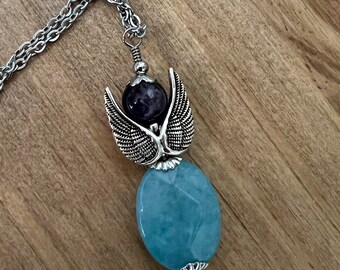 May include: A silver chain necklace with a pendant featuring a silver angel with wings holding a purple amethyst stone and a light blue aquamarine stone.