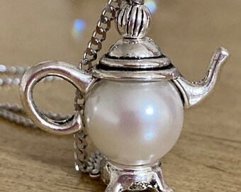 May include: A silver teapot pendant necklace with a white pearl. The teapot has a detailed design and a small handle. The necklace is on a silver chain.
