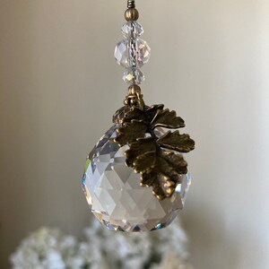 May include: A crystal ball with a gold leaf design hanging from a chain with clear crystal beads.