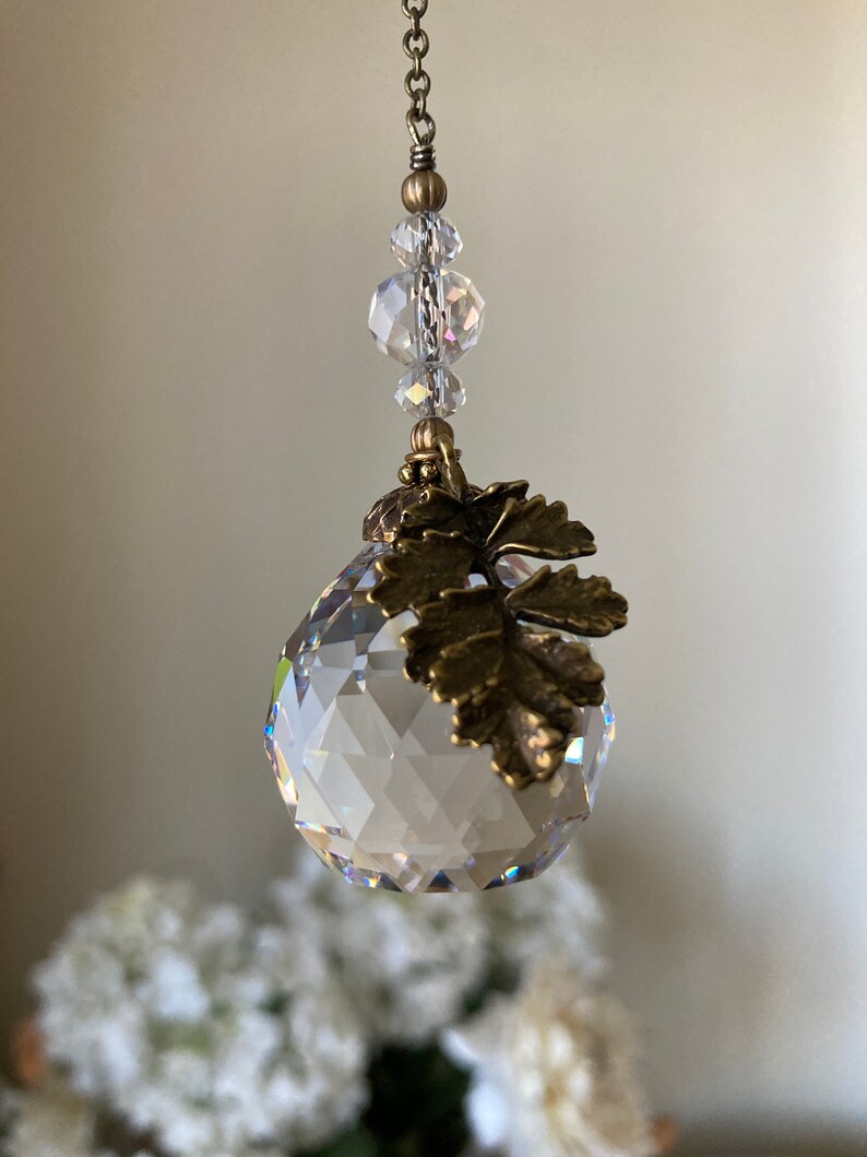 May include: A crystal ball with a gold leaf design hanging from a chain with clear crystal beads.