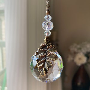 May include: A crystal suncatcher with a gold leaf design hangs from a chain with clear crystal beads.